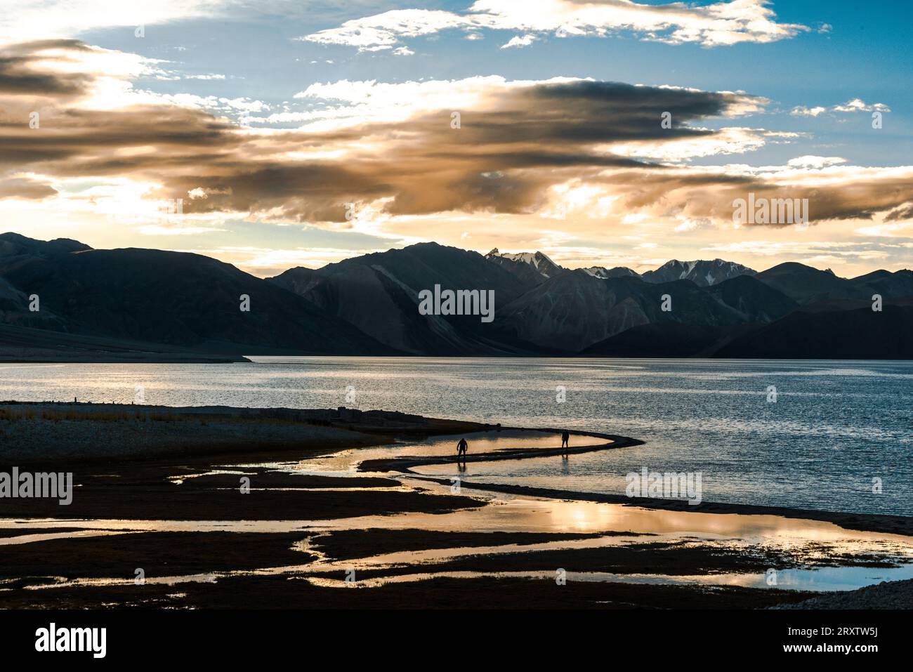 Coucher de soleil au lac Pan Gong avec réflexion de lumière dorée dans les eaux plates montrant deux personnes marchant le long de la rive, Ladakh, nord de l'Inde, Asie Banque D'Images