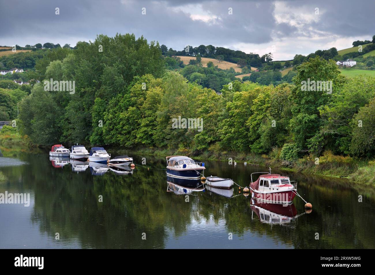 Ligne de bateaux amarrés sur la rivière Dart avec des arbres et des collines ondulantes paysage sur une journée nuageuse en été. Totnes, South Hams, South Devon, Angleterre, Royaume-Uni Banque D'Images