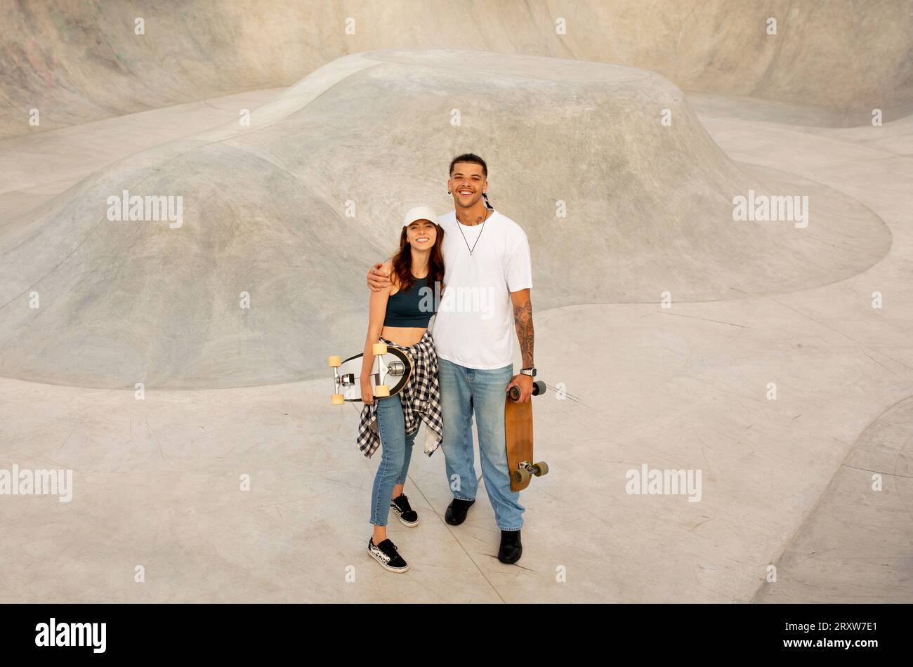 Jeune femme et gars posant avec des planches à roulettes et embrassant, se relaxant après des exercices sur rampe, pleine longueur, espace de copie Banque D'Images