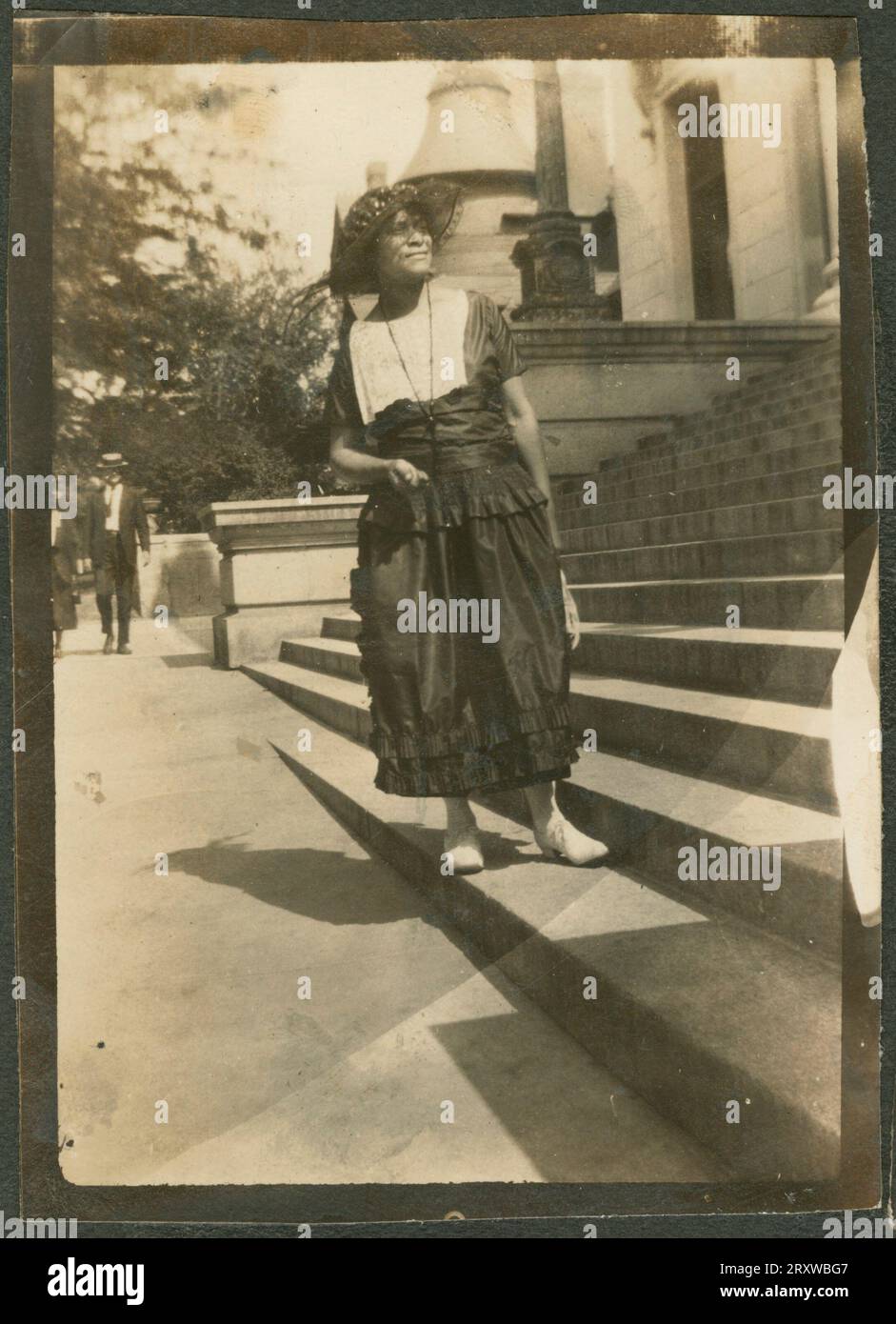 Page de l'album photo avec trois photographies - Photographie noir et blanc d'une femme portant une robe sombre avec un corsage blanc et un chapeau noir. Elle est debout sur les marches d'un grand bâtiment. Un homme et une femme peuvent être vus marchant sur un trottoir en arrière-plan. Banque D'Images