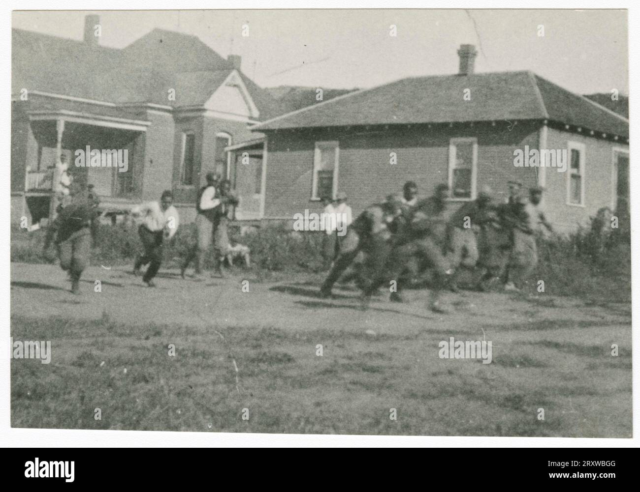 Photographie d'hommes en train de rouler avec un ballon de football devant deux maisons Banque D'Images