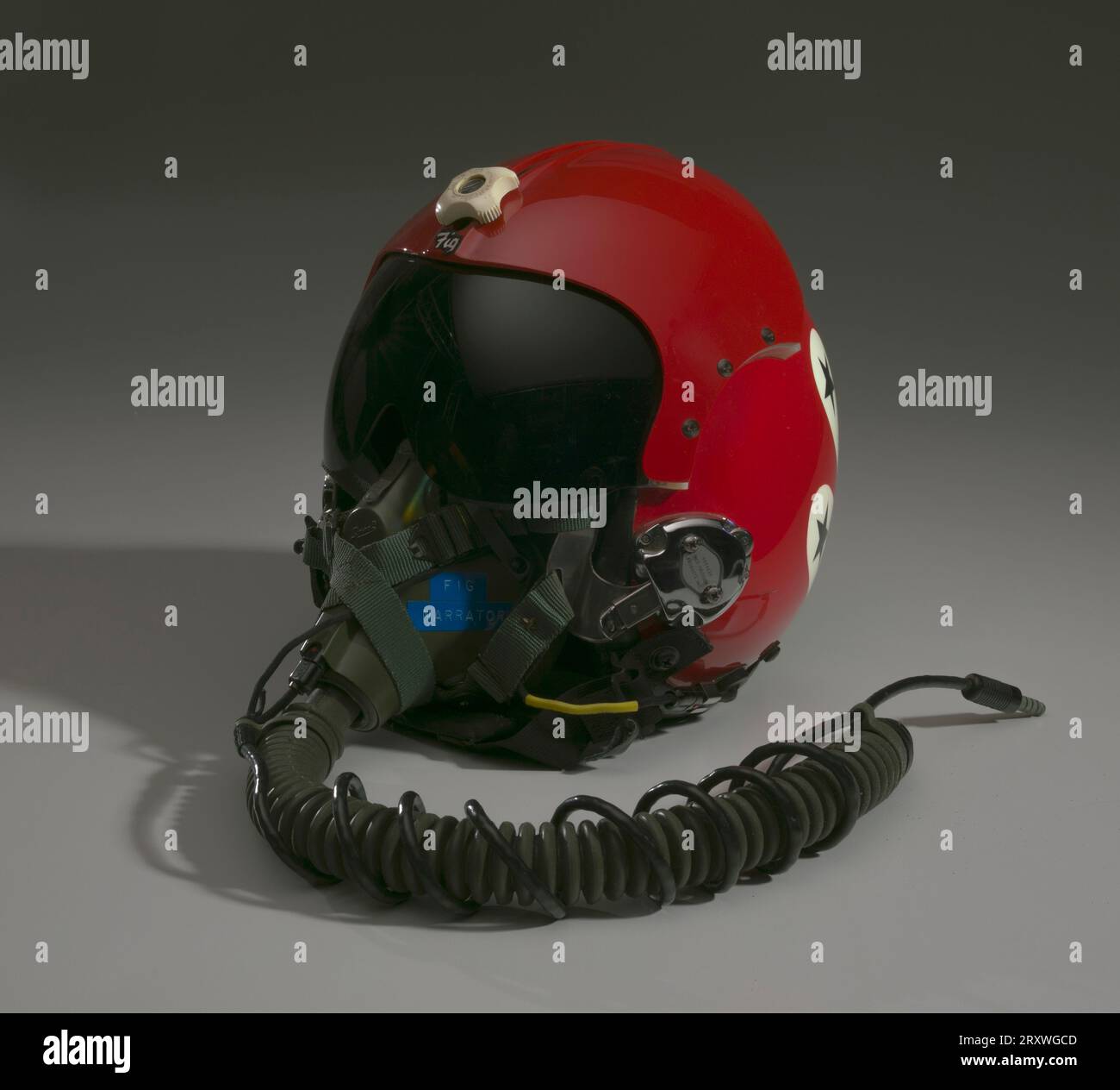 Casque de vol rouge, blanc et bleu avec visière noire. Le casque de vol est principalement rouge, avec une illustration à l'arrière. L'illustration sur casque représente un aigle avec quatre avions de chasse dans une étoile blanche en son centre. Des étoiles bleues sur fond blanc entourent l'aigle. Le type bleu sous l'aigle lit, [Thunderbirds]. Sur les côtés PR et PL du casque se trouvent des mécanismes métalliques auxquels le masque à oxygène de vol se fixe. Tapez sur chacun des mécanismes, [60C4459/IMCO PRECISION/PRODUCTS Inc.]. Peint au centre de l'avant du casque est [Fig]. La visière du casque est réglable à l'aide d'un bouton blanc. Banque D'Images