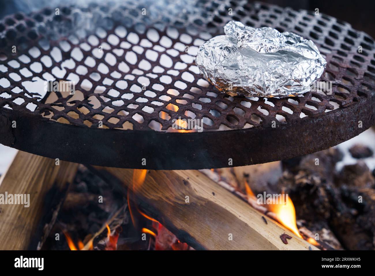 En hiver, des aliments enveloppés de papier d'aluminium sur un grill au-dessus du feu de camp. Banque D'Images