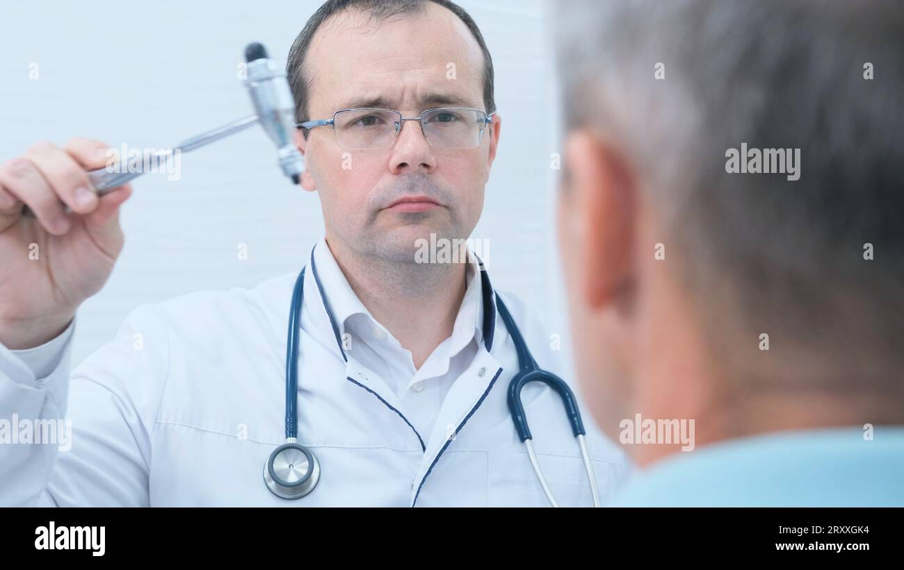 Un neurologue examine le système nerveux et les réflexes d'un patient masculin avec un marteau neurologique dans une clinique médicale. L'examen neurologique. Banque D'Images