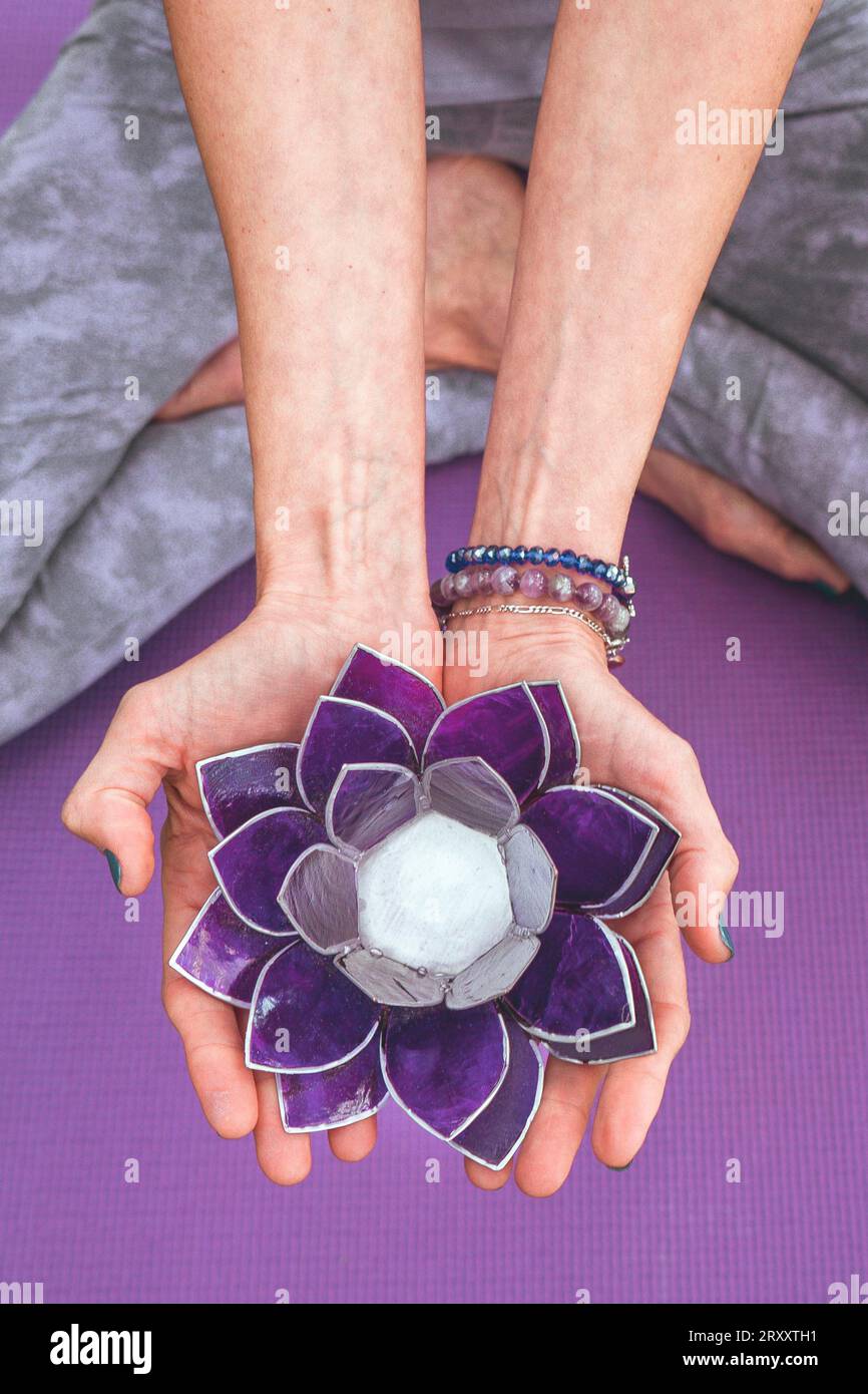 Vue d'angle de dessus des mains tenant un lotus en verre violet. Concept de yoga et de méditation. Tir vertical Banque D'Images