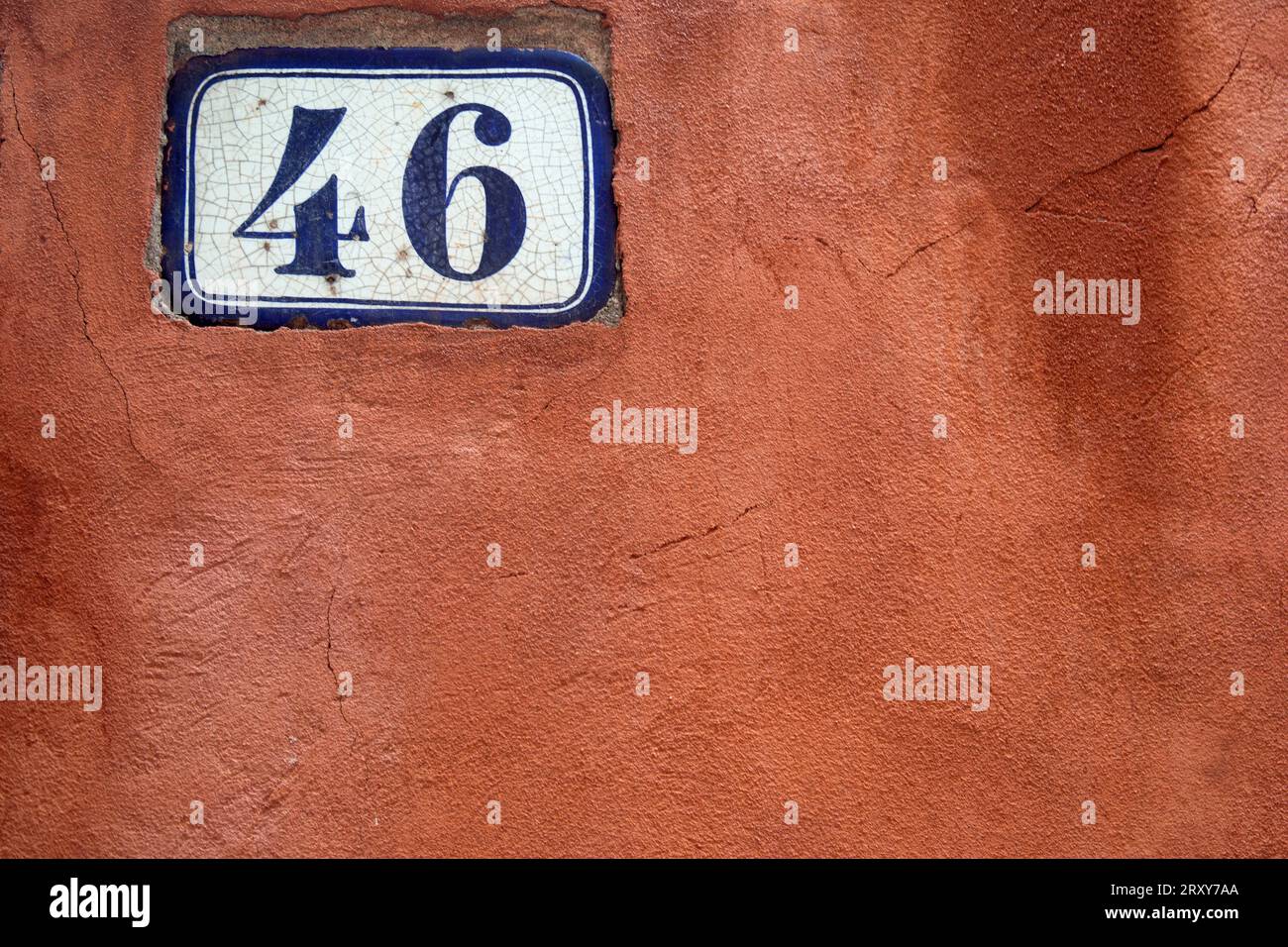 Le numéro 46 en bleu foncé sur un panneau blanc contre un mur peint en rouge, photographié en gros plan remplissant le cadre mais laissant l'espace de copie. Banque D'Images