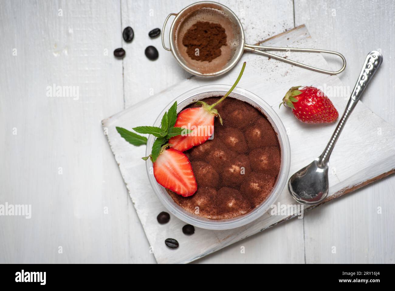 Dessert sucré italien traditionnel de gâteau tiramisu en verre sur une table en bois blanc. Avec fraise et cacao en poudre Banque D'Images