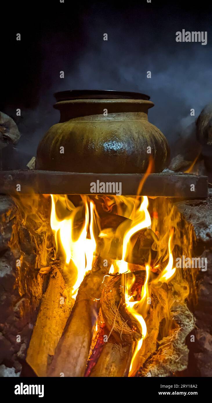 une bouilloire brune avec de la nourriture cuite et fumée sous le feu dans un vieux poêle traditionnel brûlant avec du bois de chauffage Banque D'Images