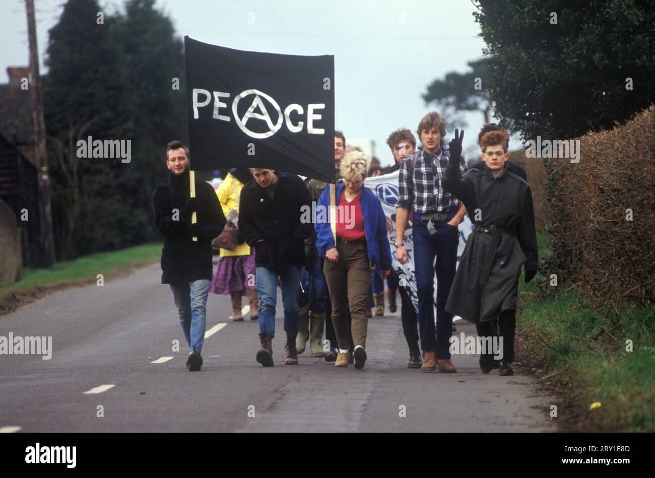 Jeunes anarchistes manifestants de la paix marchent d'Aldermaston à Greenham Common vendredi Saint Pâques 1983. Les manifestants pour la paix (pas ce groupe) formaient une chaîne humaine qui s'étendait sur 14 milles. Ils ont tracé une route le long de ce que les manifestants appellent la "Nuclear Valley" dans le Berkshire. La chaîne a commencé à la base aérienne américaine de Greenham Common, a dépassé le centre de recherche nucléaire d'Aldermaston et s'est terminée à l'usine de munitions de Burghfield. Un jeune anarchiste fait un geste de la main au Salut de la paix. ANNÉES 1980 ROYAUME-UNI HOMER SYKES Banque D'Images