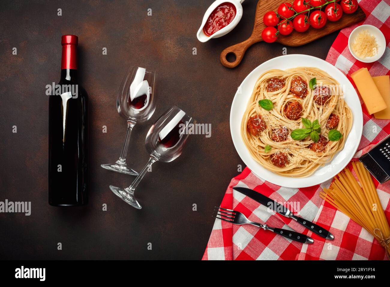 Pâtes spaghetti avec boulettes de viande, sauce tomate cerise, fromage, verre à vin et bouteille sur fond rouillé, vue de dessus. Banque D'Images