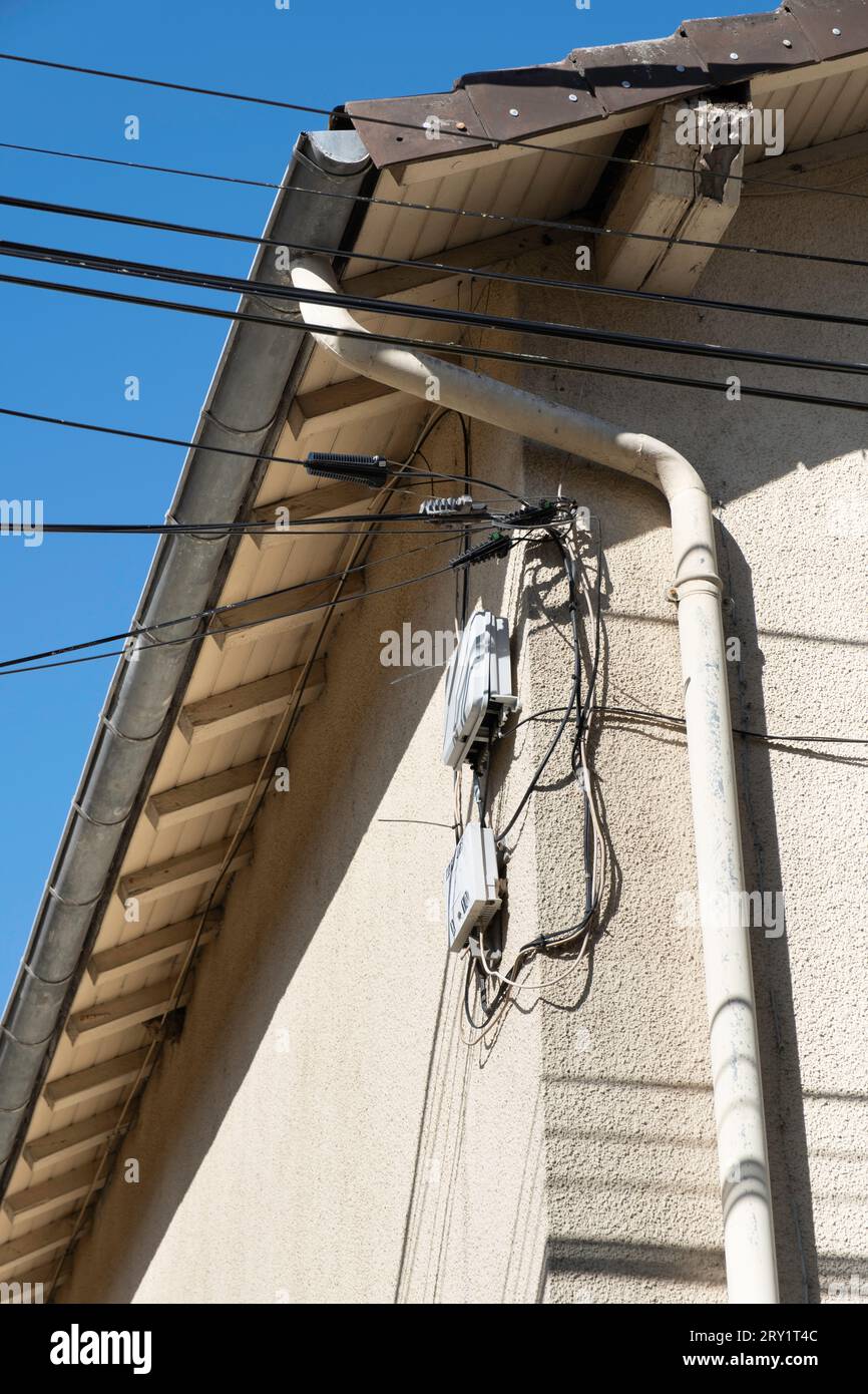 Boîtiers de câblage et de commande pour le téléphone, les données et l'électricité ouverts et visibles le long d'un tuyau d'évacuation contre un mur plâtré d'une maison en France Banque D'Images