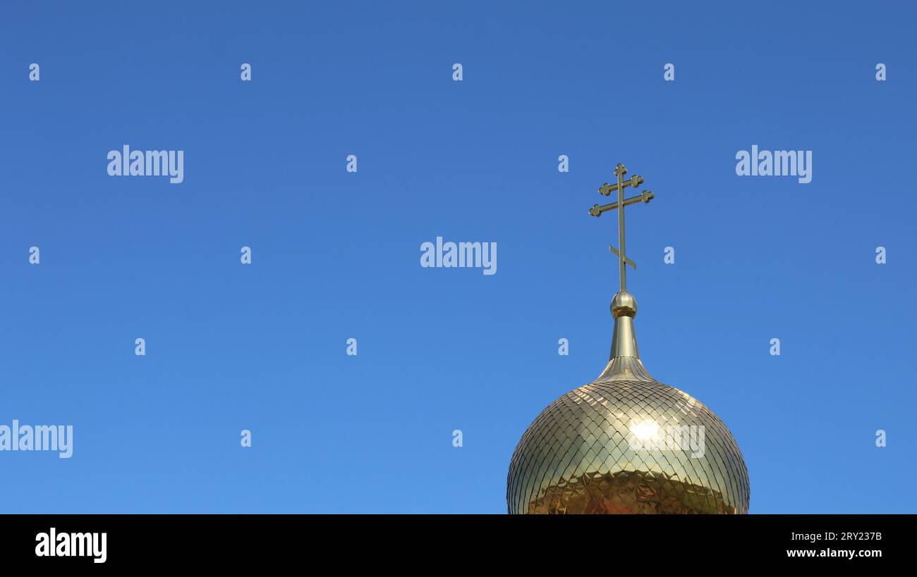 dôme doré d'une église orthodoxe avec une élégante croix sur un ciel bleu clair comme un fond religieux avec un espace pour l'insertion Banque D'Images