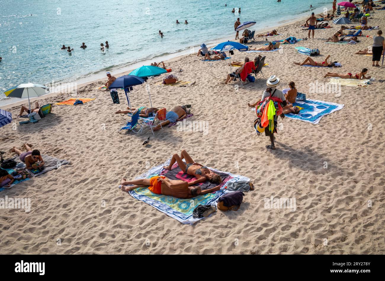 Un vendeur de plage passe devant des gens se détendant sur la plage publique de Zamenhof à Cannes sur la Côte d'Azur dans le sud de la France. Banque D'Images