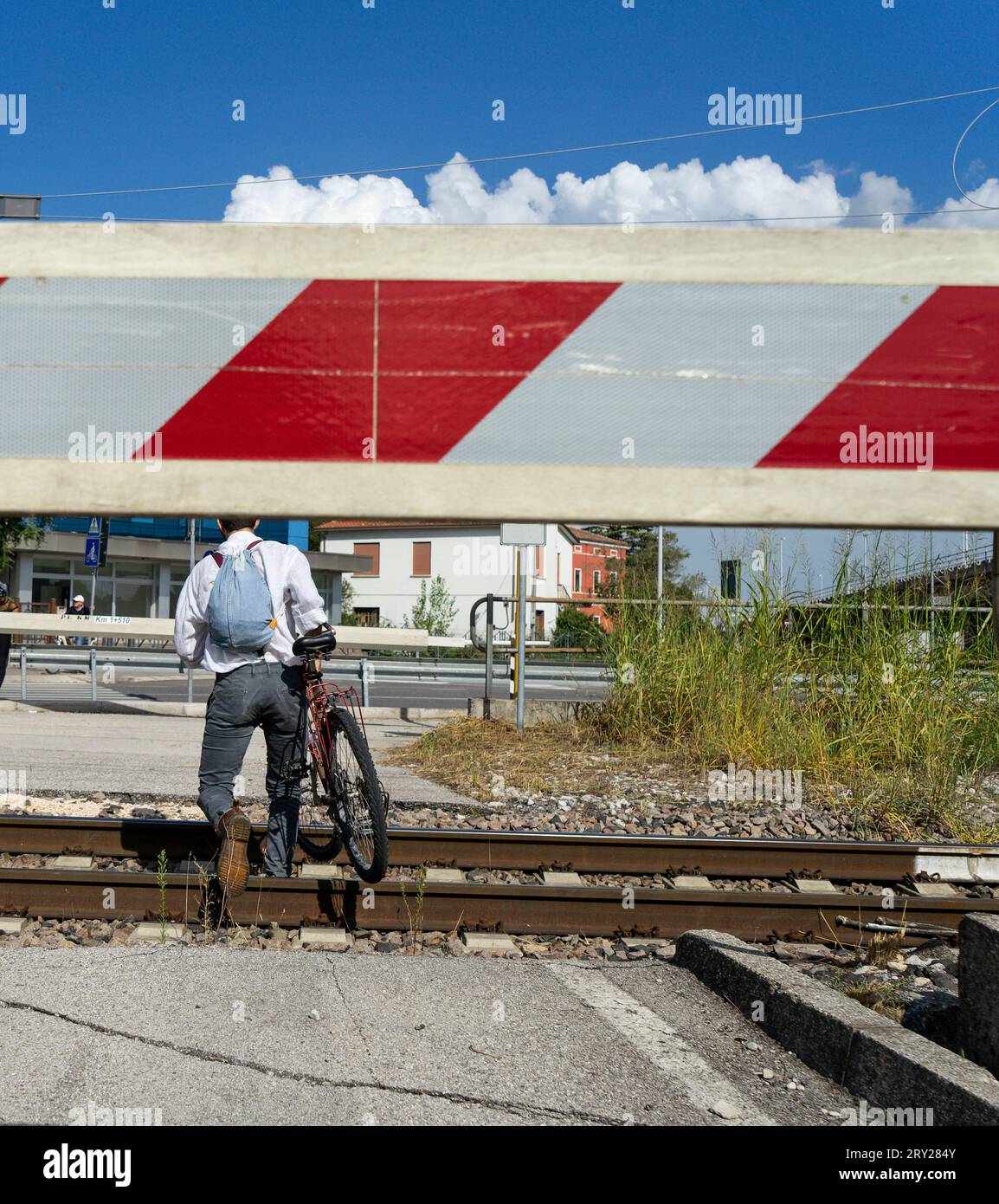 Un homme à bicyclette traverse les voies ferrées tandis que la barre de croisement est abaissée à un passage à niveau télécommandé Banque D'Images