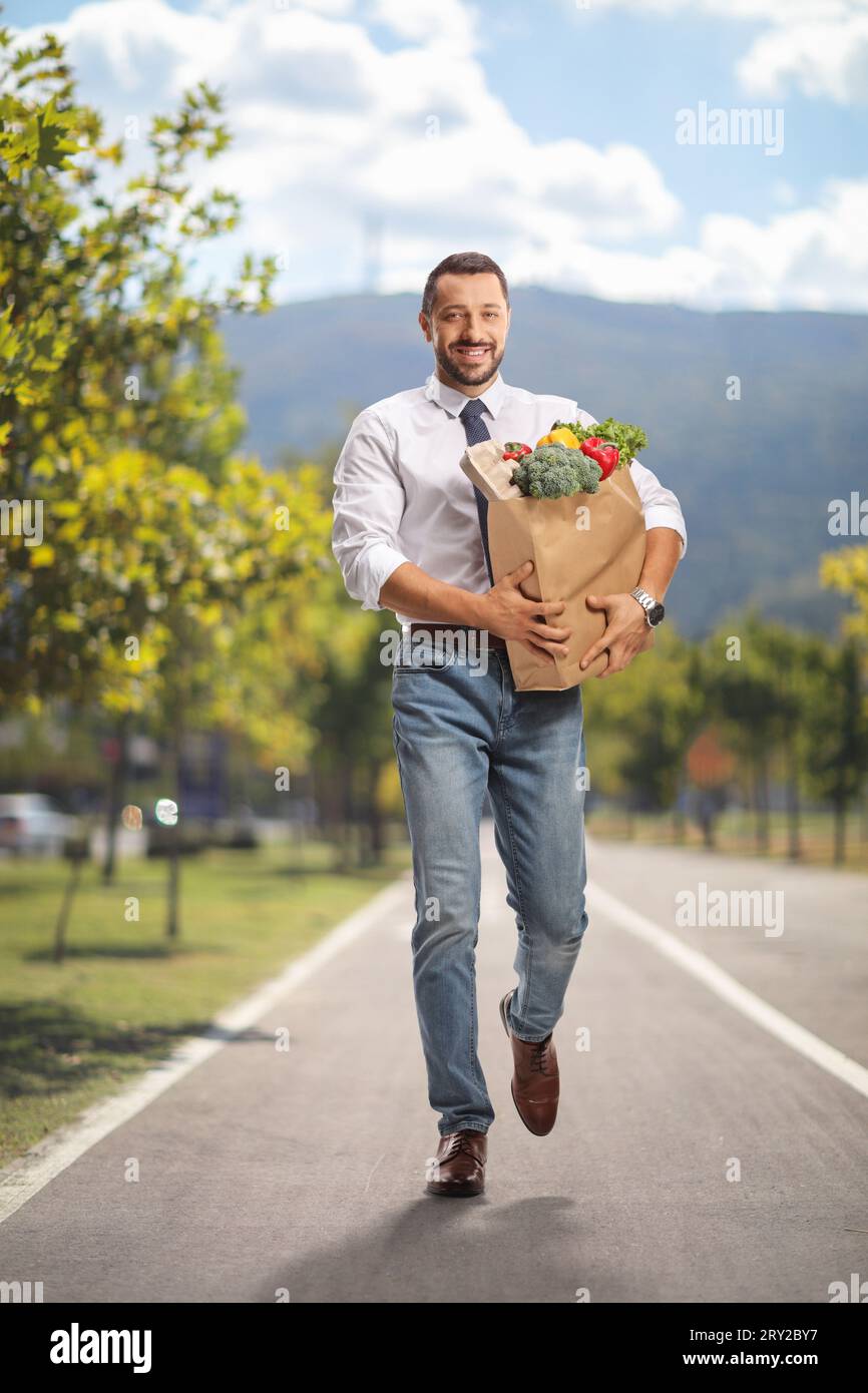 Portrait en pied d'un jeune homme professionnel portant un sac d'épicerie et marchant dans une voie piétonne Banque D'Images