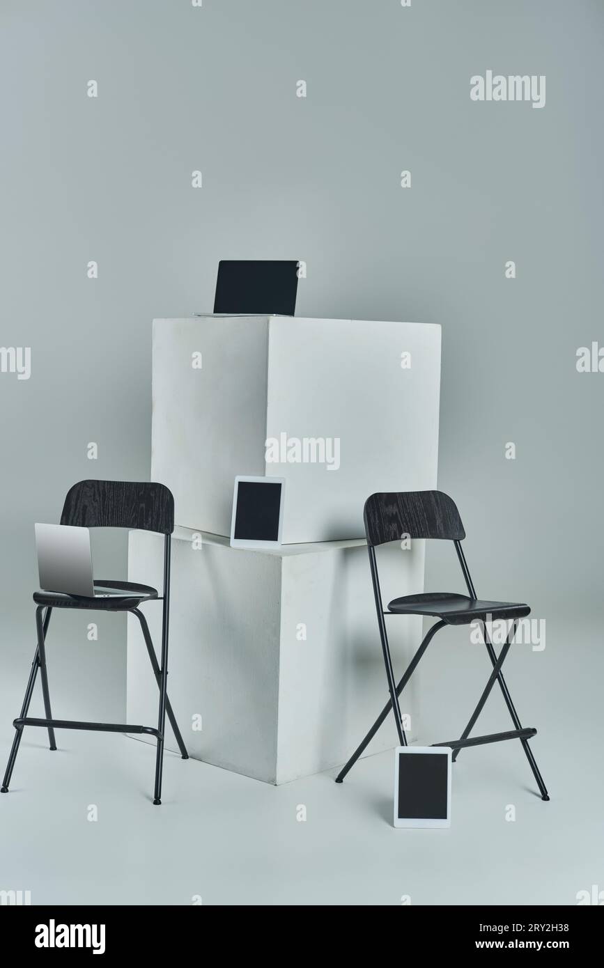 ordinateurs portables et tablettes numériques avec écran vierge près de cubes blancs et chaises de bureau sur fond gris Banque D'Images