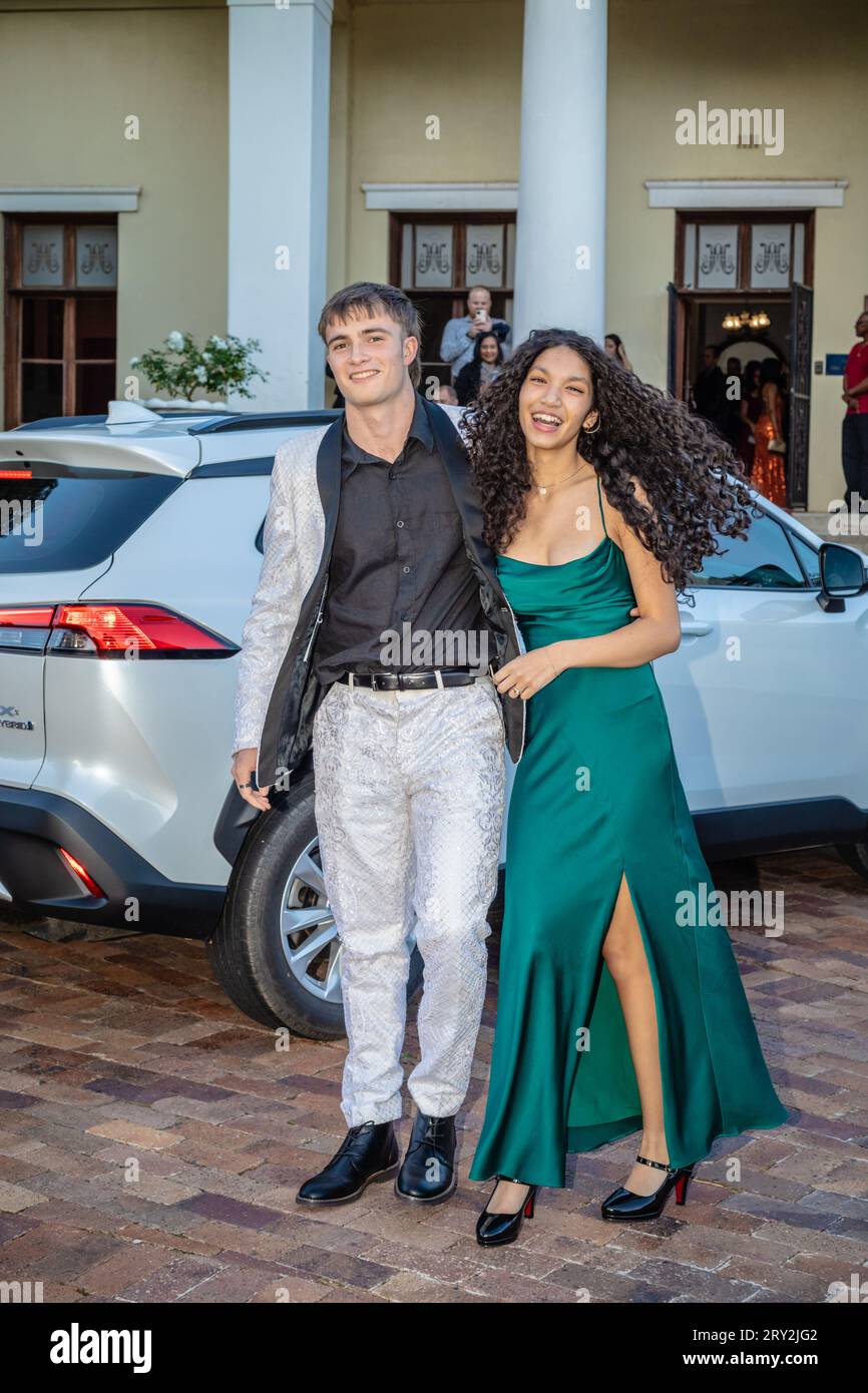 Un couple multiracial fait une grande entrée au bal de promo, en sortant avec style avec une voiture blanche élégante derrière eux, exsudant l'élégance Banque D'Images