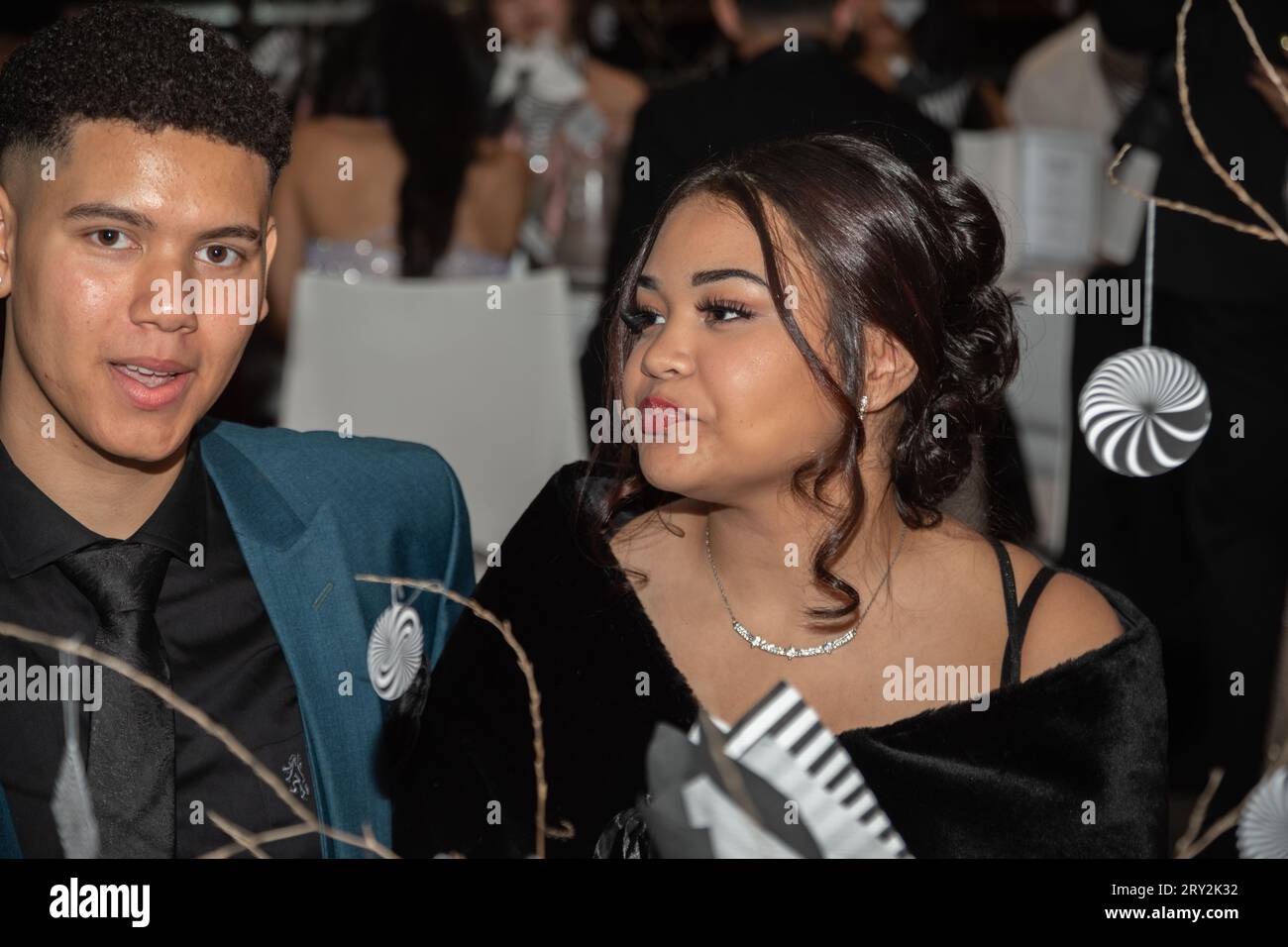 Au bal de promo, un jeune couple s'assoit à une table joliment décorée, perdu dans un monde d'élégance et de romantisme. Banque D'Images