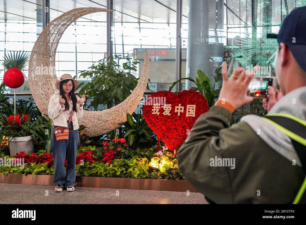 Pékin, province chinoise du Yunnan. 27 septembre 2023. Un passager pose pour des photos devant des décorations florales à l'aéroport international de Kunming Changshui à Kunming, dans la province du Yunnan, dans le sud-ouest de la Chine, le 27 septembre 2023. La période des fêtes de la mi-automne et de la fête nationale, qui durera du 29 septembre au 6 octobre cette année, est une saison touristique et touristique de pointe en Chine. Crédit : Cui Wen/Xinhua/Alamy Live News Banque D'Images