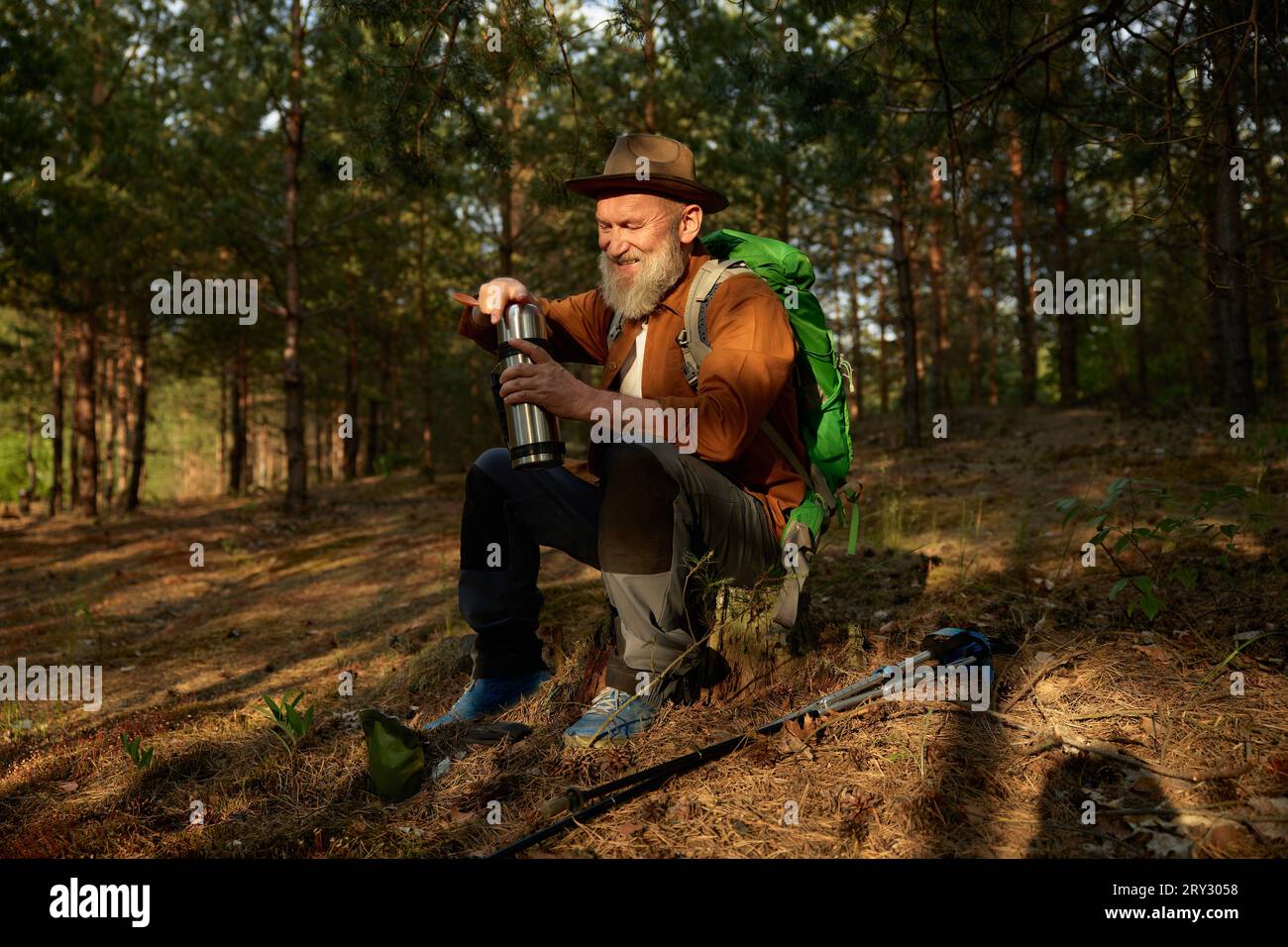 Homme senior randonneur buvant du thé chaud de la tasse thermos dans la forêt Banque D'Images