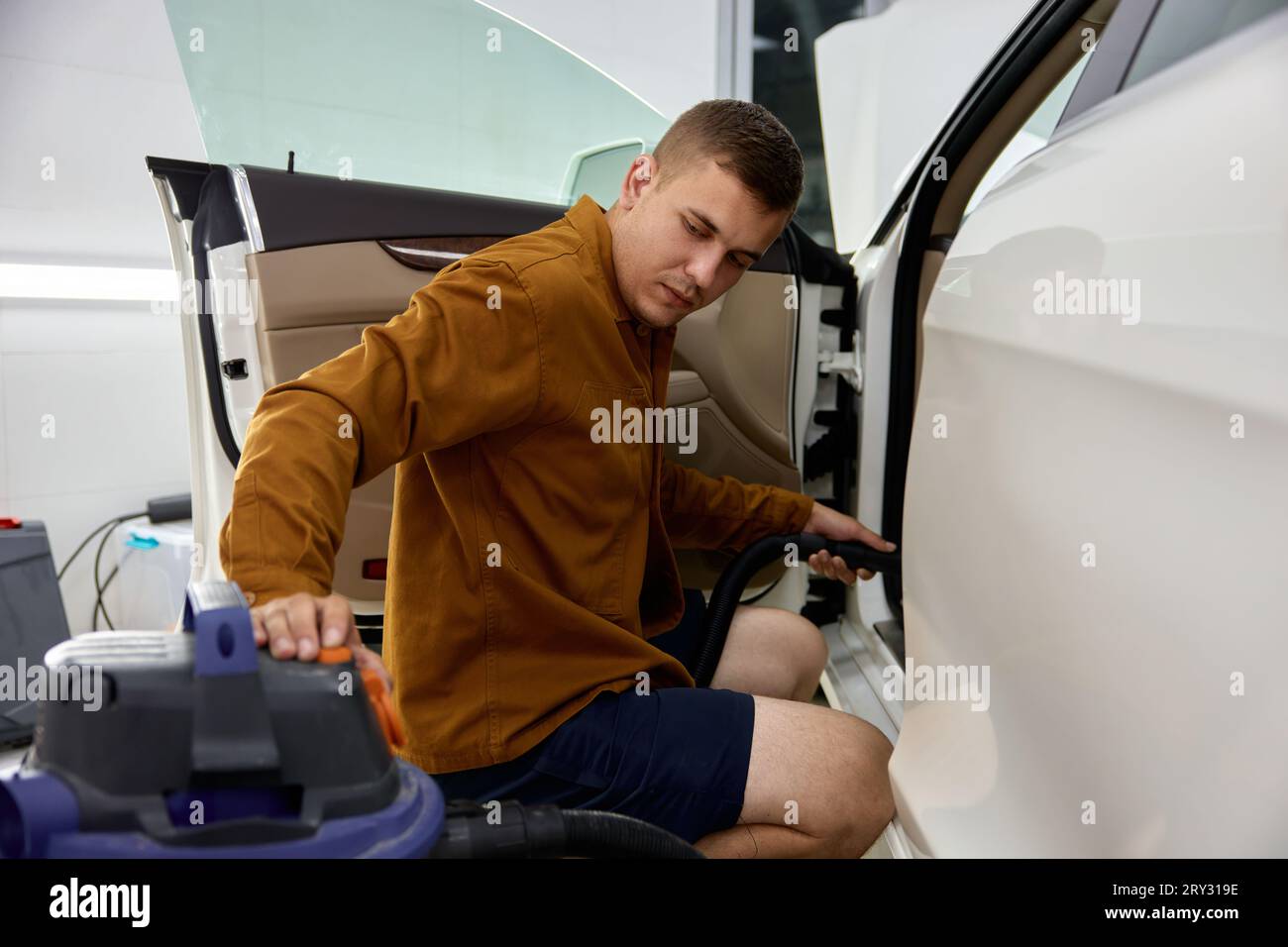 Homme engagé dans le nettoyage à sec de l'intérieur de la voiture en utilisant la machine de ventilateur d'aspiration Banque D'Images