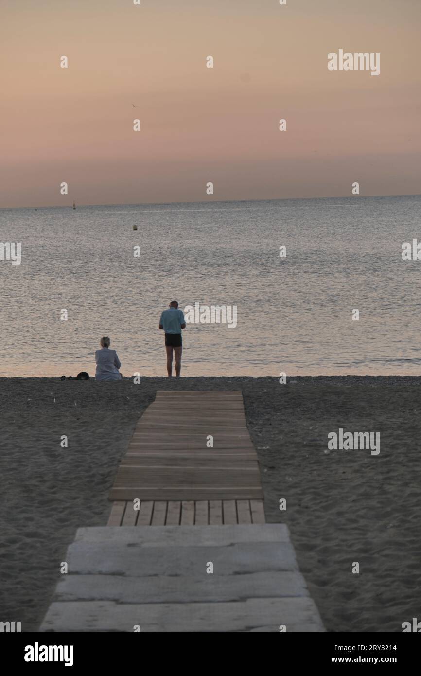 Couple au bout de la passerelle sur le sable au lever du soleil de la mer Banque D'Images