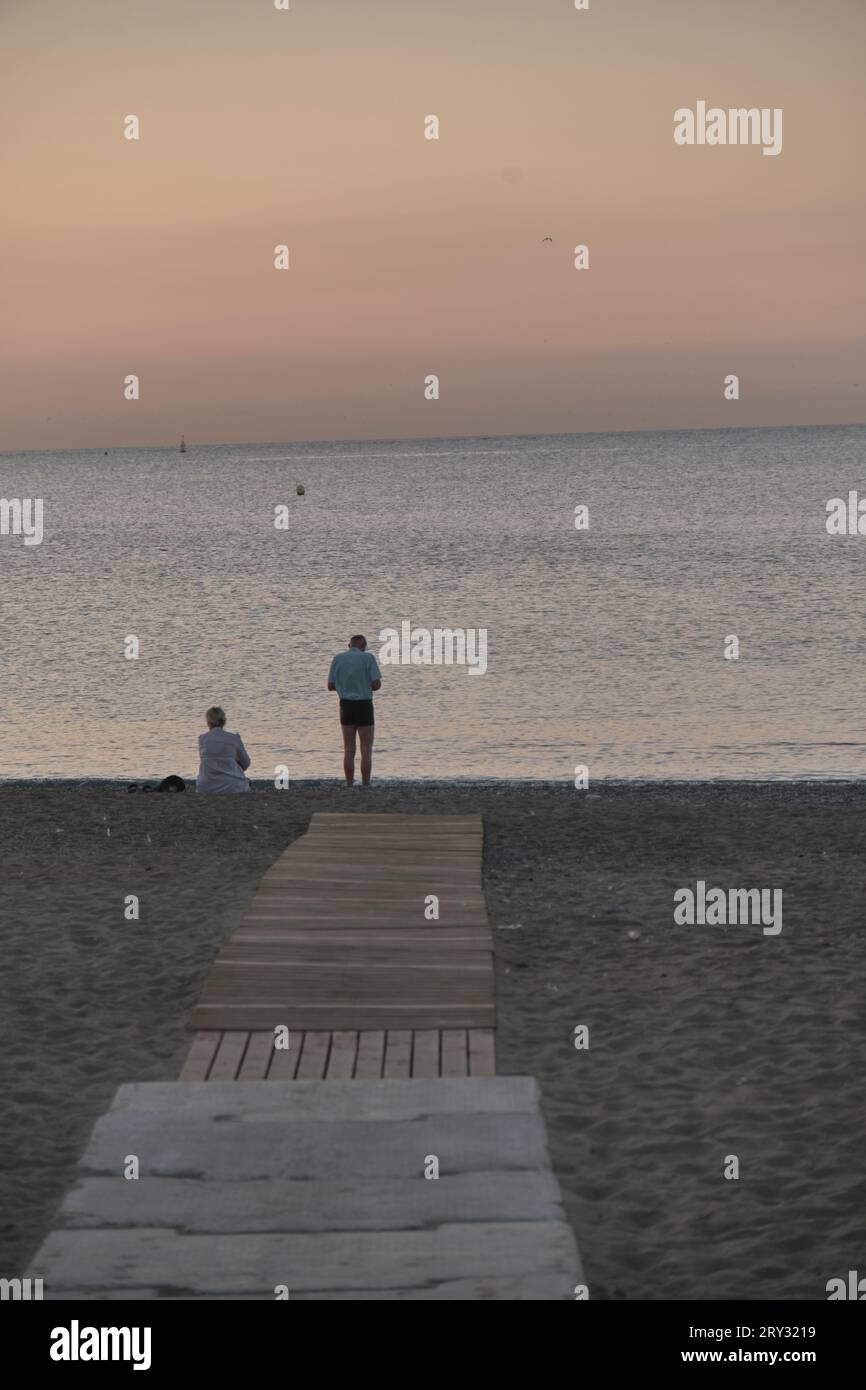 Couple au bout de la passerelle sur le sable au lever du soleil de la mer Banque D'Images