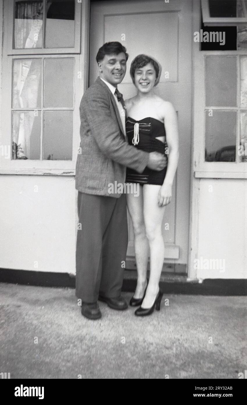 Années 1960, historique, un jeune couple heureux debout pour une photo devant leur chalet de vacances, la jeune femme en maillot de bain de l'époque, Angleterre, Royaume-Uni. Banque D'Images
