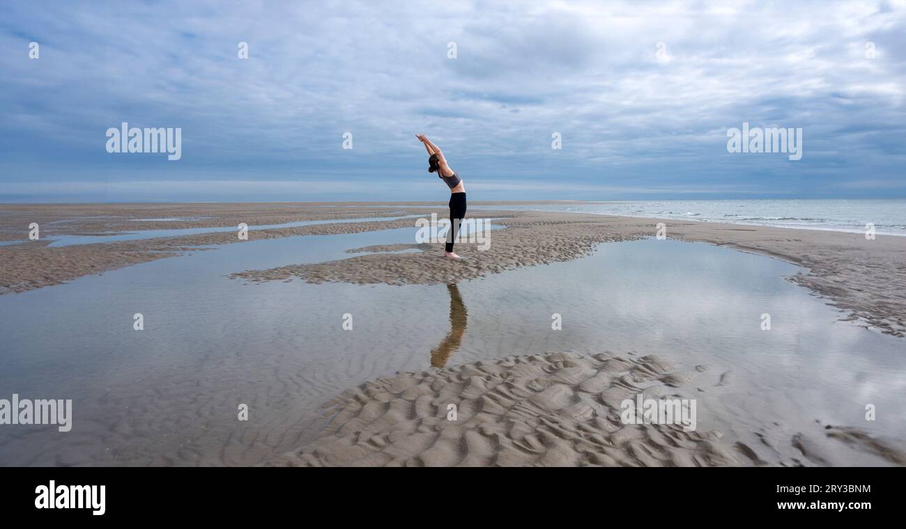 femme sportive s'étirant et s'entraînant sur une plage à marée basse Banque D'Images