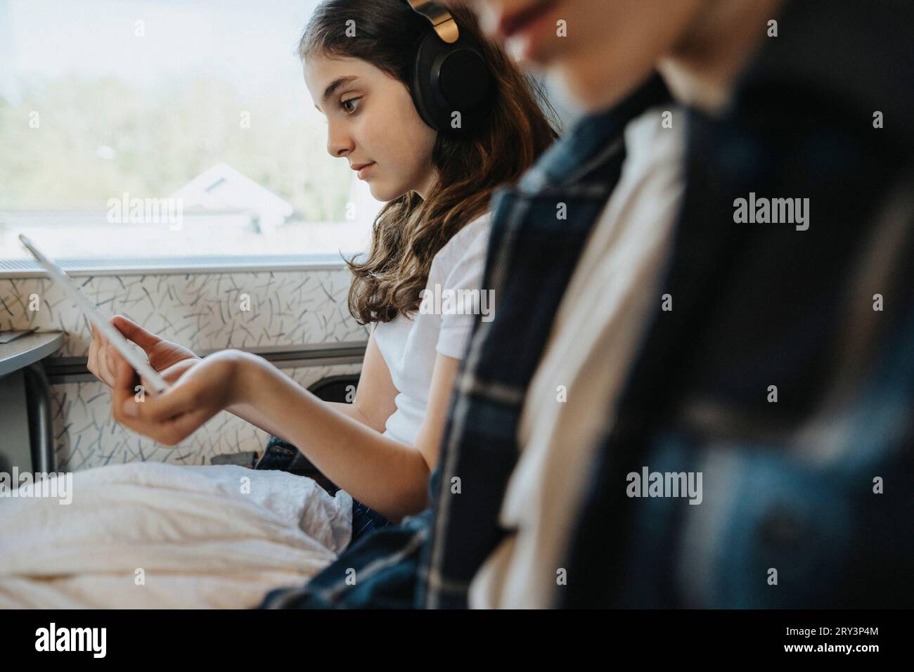 Fille portant un casque bluetooth tout en regardant Tablet PC dans le train Banque D'Images