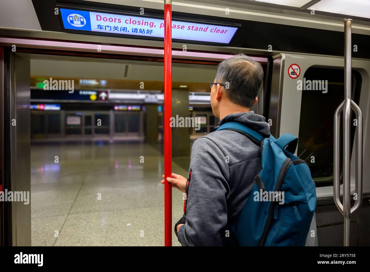 Homme debout près de la porte ouverte de la liaison ferroviaire de l'aéroport. Le tableau au néon au-dessus avec des messages en anglais et chinois - fermeture des portes, s'il vous plaît debout cle Banque D'Images