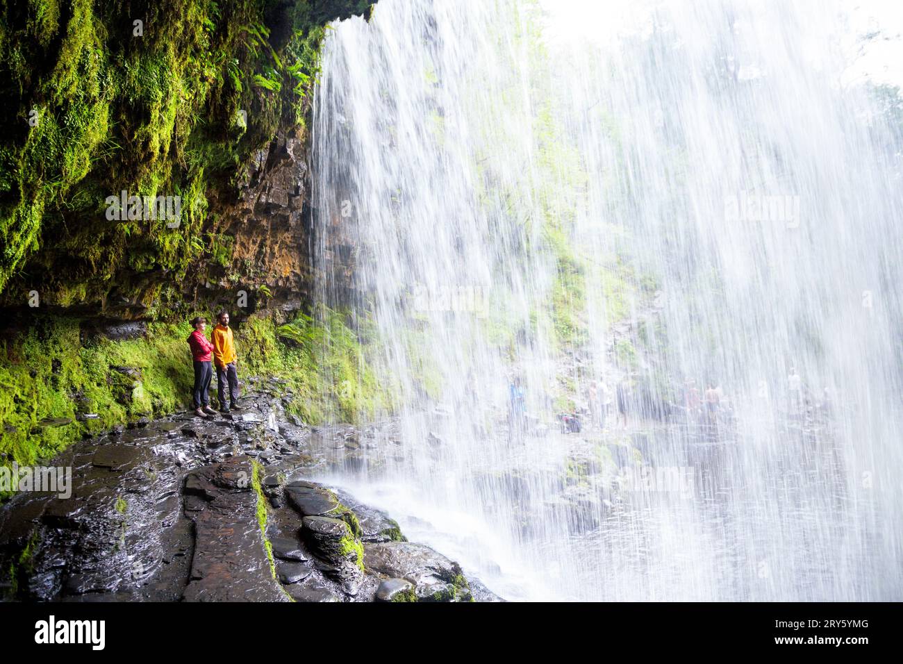 Personnes debout derrière Sgwd yr Eira Waterfall, four Waterfalls Walk, Brecon Beacons National Park, pays de Galles, Royaume-Uni Banque D'Images