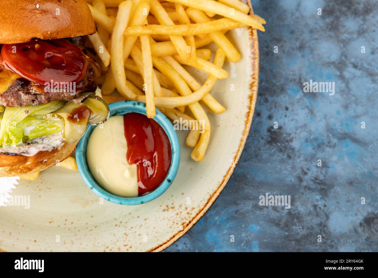 Burger de bœuf avec laitue et cornichons avec frites et sauce sur fond gris-bleu. Service de restauration Banque D'Images