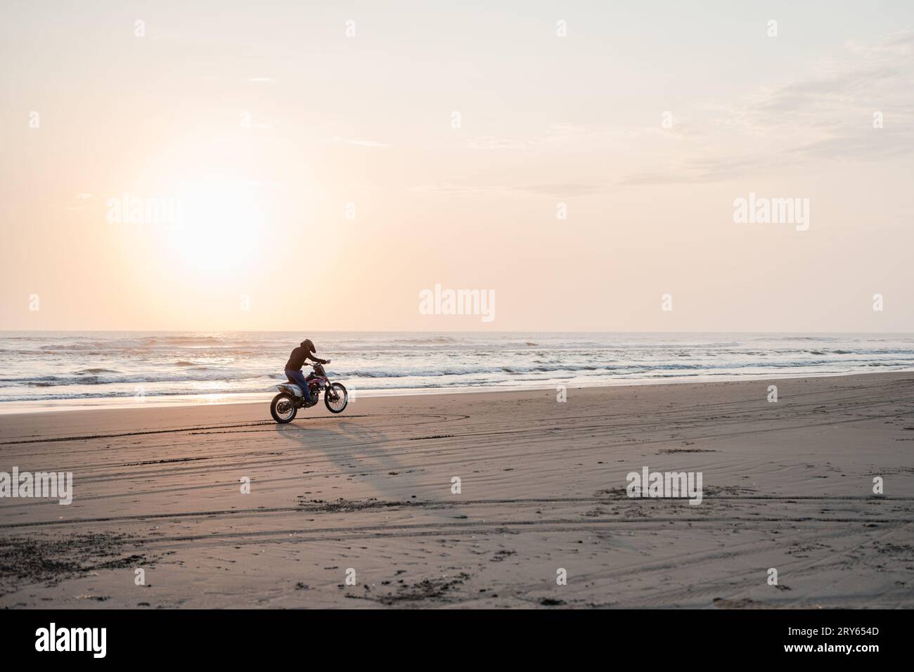 Pilote de motocross conduisant le long de la plage au coucher du soleil Banque D'Images