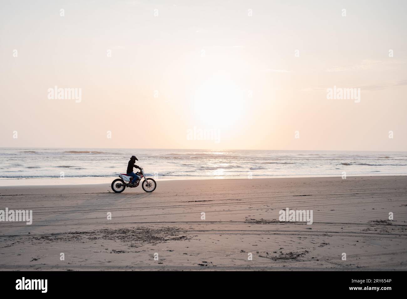 Pilote de motocross conduisant le long de la plage au coucher du soleil Banque D'Images