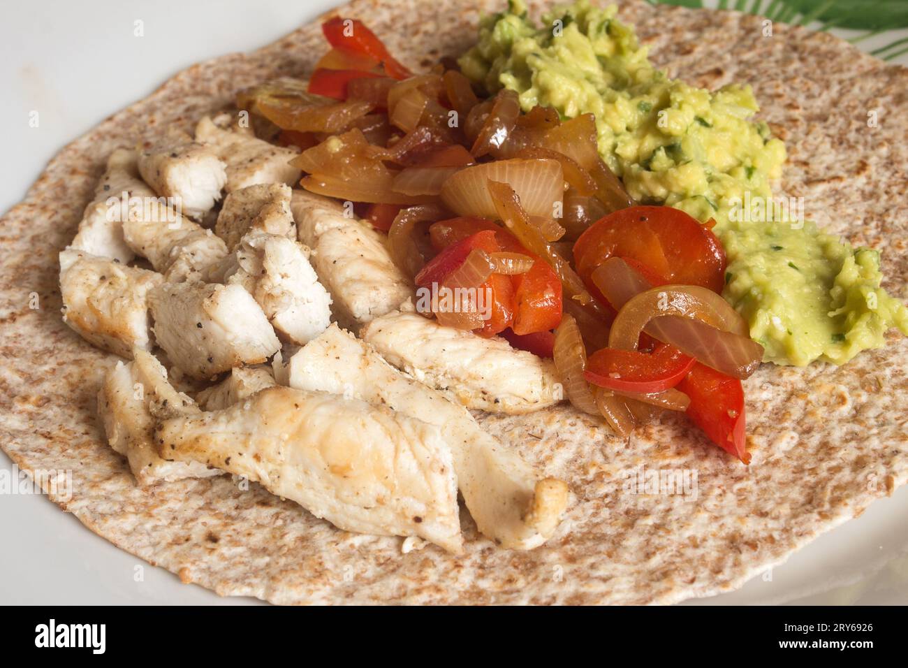 Une tortilla fajita au poulet de blé entier avec du poulet assaisonné au cumin, des légumes verts croustillants et du guacamole maison dans une cuisine rustique. Cuisine mexicaine. Banque D'Images