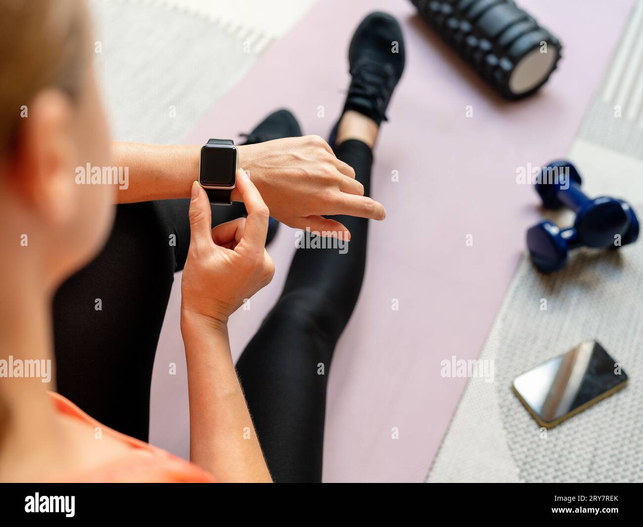 Vue à grand angle sur la montre intelligente de sport avec écran blanc sur le poignet de l'athlète féminine assis sur le tapis d'exercice à la maison. Banque D'Images