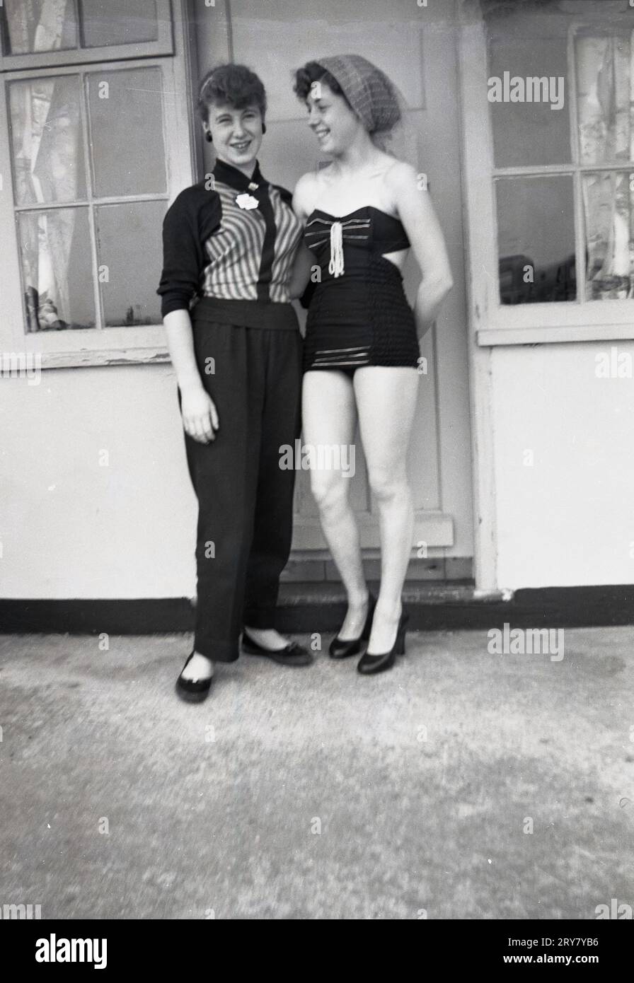 Années 1960, historique, deux jeunes femmes, sœurs, debout togther pour une photo à l'extérieur de leur chalet dans un camp de vacances, l'une d'elles portant un maillot de bain de l'époque, Angleterre, Royaume-Uni. Banque D'Images