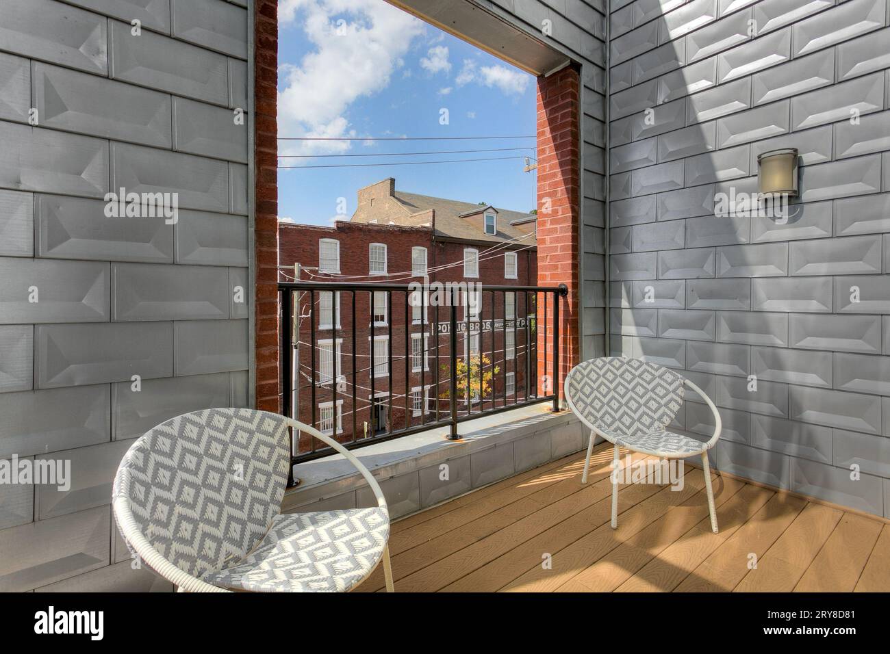 Mur d'accent métallique sur balcon extérieur avec chaises longues avec ouverture moderne ouverte avec bâtiment en briques historique et ciel bleu Banque D'Images