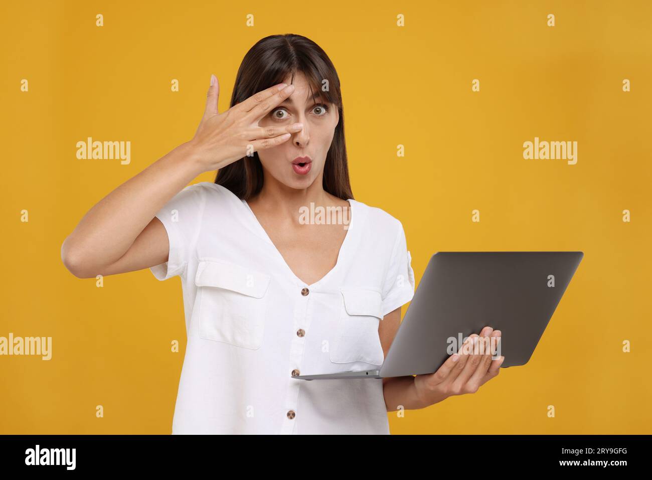 Femme embarrassée avec ordinateur portable couvrant le visage sur fond orange Banque D'Images