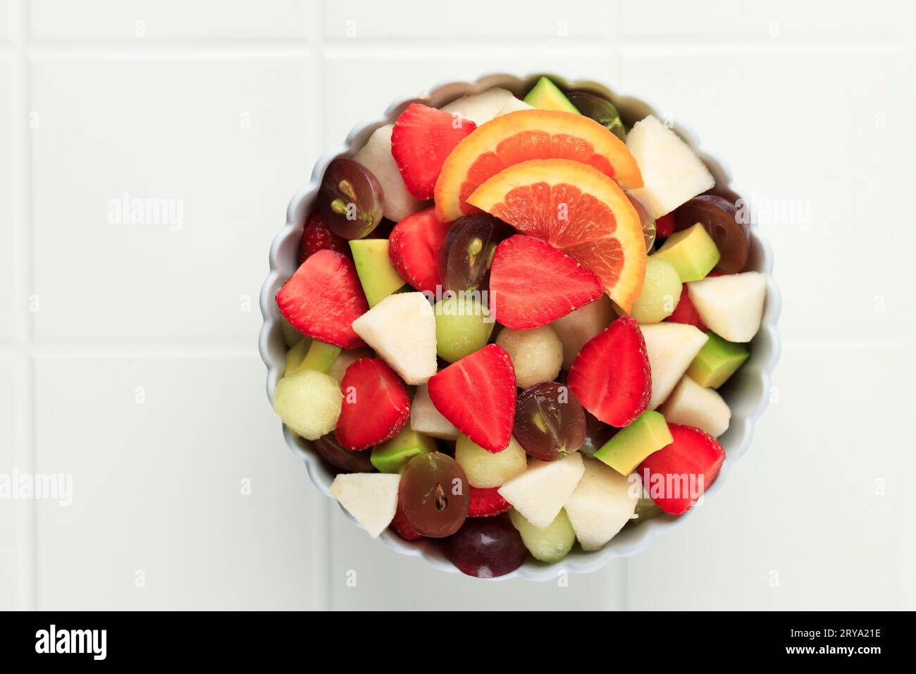 Vue de dessus salade de fruits frais dans le bol, fraise de fruits tranchés, poire, raisin, avocat et pamplemousse orange sur la table blanche Banque D'Images
