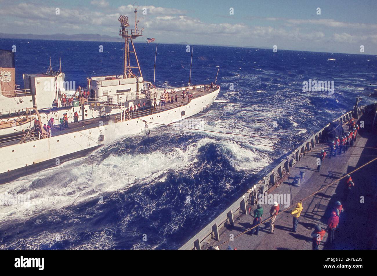 Un navire de la Garde côtière et un navire de la Marine, chacun en mouvement, font un exercice de transfert d'un passager d'un navire à un autre. Un mannequin est utilisé à la place pour la perceuse. Cette photo de 1971 a été prise depuis l'USS Compass Island, un navire de recherche. Banque D'Images