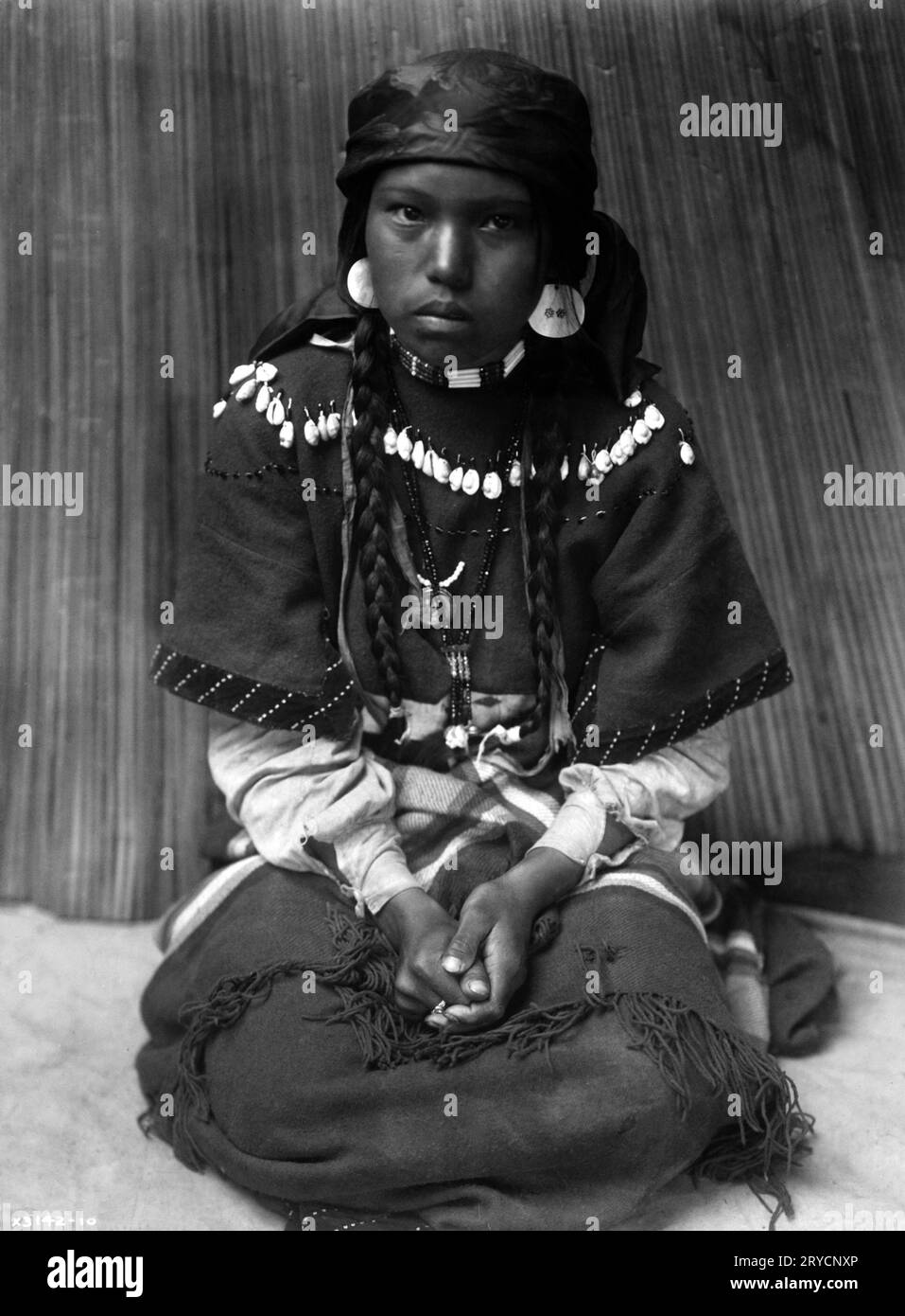 Kalispel Girl par Edward S. Curtis, ca. 1910 fille Kalispel (ou Pend d'oreilles) assise sur ses genoux, les mains pliées sur les genoux, sous-titrée 'Touch her dress--Kalispel'. Photographie d'Edward S. Curtis, ca. 1910. Banque D'Images