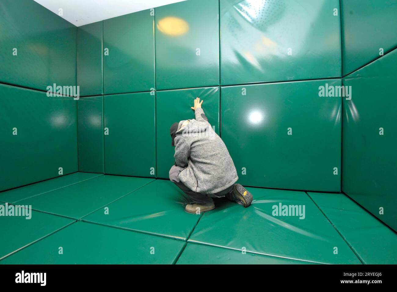 Homme agenouillé dans une cellule rembourrée verte Banque D'Images