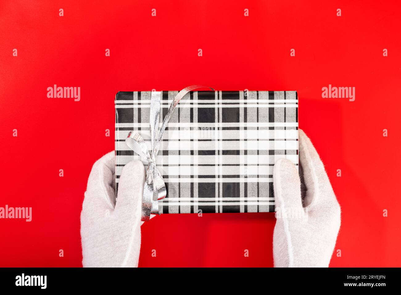 Père Noël avec des mains gantées tenant un cadeau de Noël sur fond rouge Banque D'Images