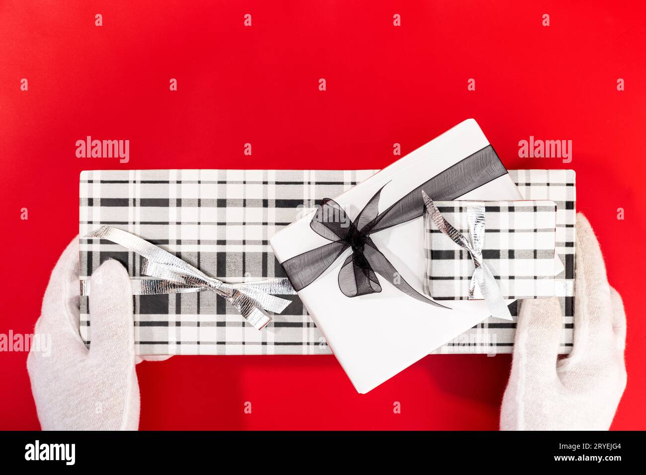 Mains gantées blanches tenant un cadeau de Noël sur fond rouge Banque D'Images