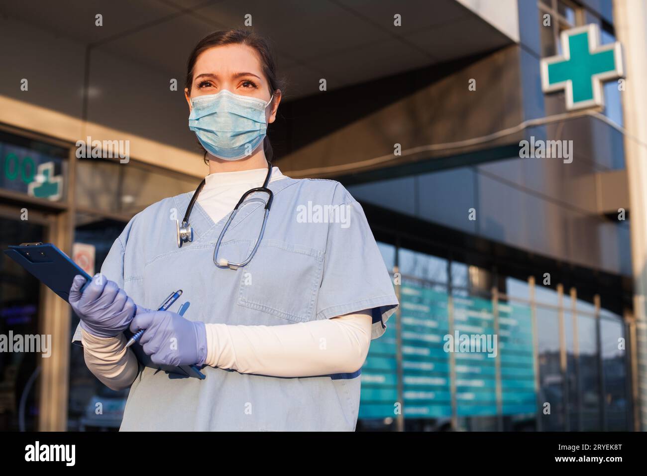 Jeune femme médecin debout devant l'établissement de santé, portant un masque facial de protection et un EPI e Banque D'Images