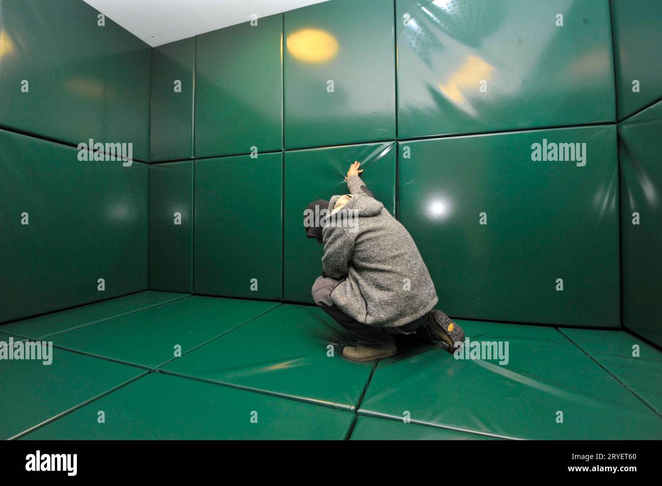 un homme s'agenouille seul dans une cellule rembourrée verte Banque D'Images