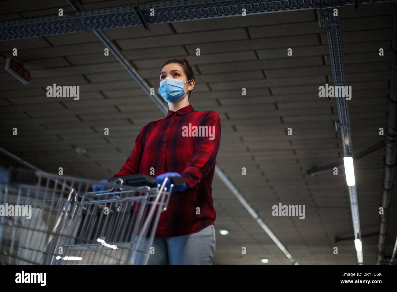 Jeune femme portant un masque poussant un chariot de supermarché dans un garage souterrain Banque D'Images