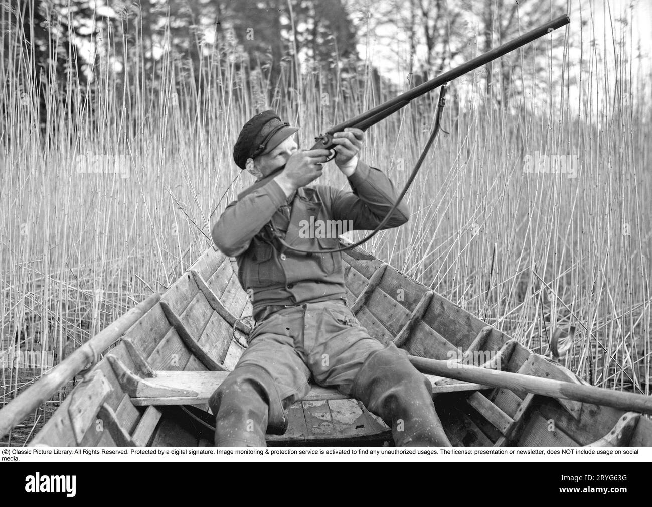 Dans les années 1930 Un homme est assis dans un bateau à rames et vise son fusil vers le haut pour tirer des canards. Suède 1939. Kristoffersson ref 155-11 Banque D'Images